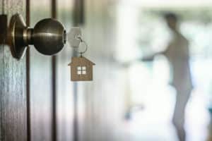 House key with home keyring in keyhole on wood door, copy space