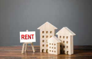 Three figures of houses and an easel with the word rent. Realtor services, search for optimal options. The concept of temporary rental housing and real estate. The choice between renting and buying.